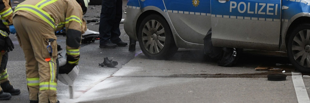 Ein Polizist und Feuerwehrmänner arbeiten an einem Unfallort, an dem ein Polizeifahrzeug während eines Einsatzes mit einem weiteren Auto zusammenprallte.