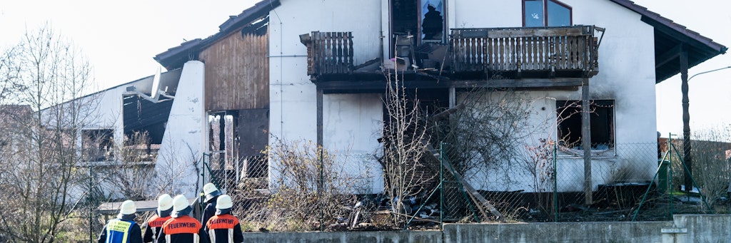 Feuerwehrleute stehen vor dem aus- gebrannten Einfamilienhaus in Bodenkirchen in Bayern.