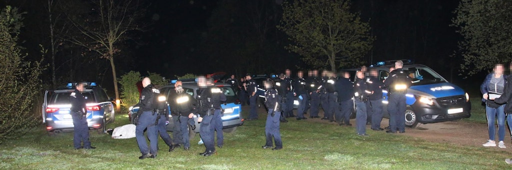 Über 20 Einsatzkräfte der Berliner Polizei stehen in einer Grünanlag am Drusenheimer Weg im Neuköllner Ortsteil Buckow. Links im Bild liegt der festgenommene Mann auf dem Rasen. 