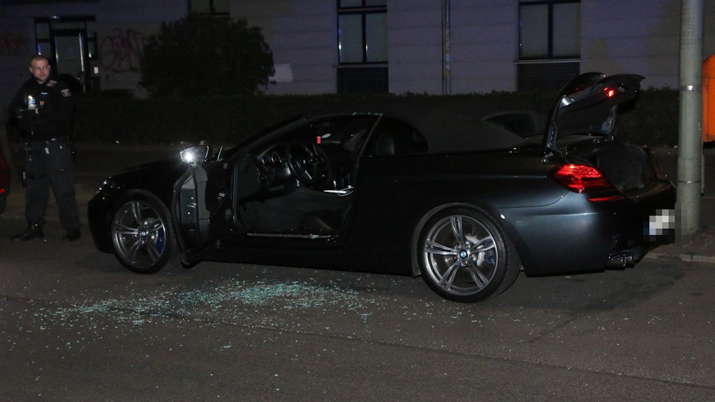 Ein Polizeibeater neben dem beschädigtem BMW in Neukölln.