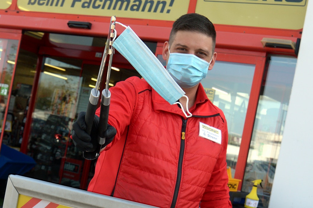 Nach wochenlanger Schließung verteilt ein Mitarbeiter eines Baumarkts in Österreich am ersten Verkaufstag Mund- und Nasenschutzmasken am Eingang. Diese sind in Geschäften Pflicht.