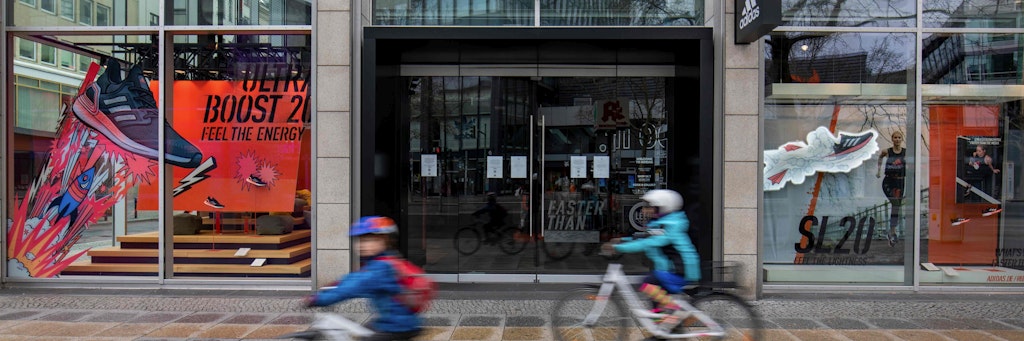 Zwei Kinder fahren mit ihren Rädern an einer geschlossenen Adidas-Filiale in Berlin vorbei. 