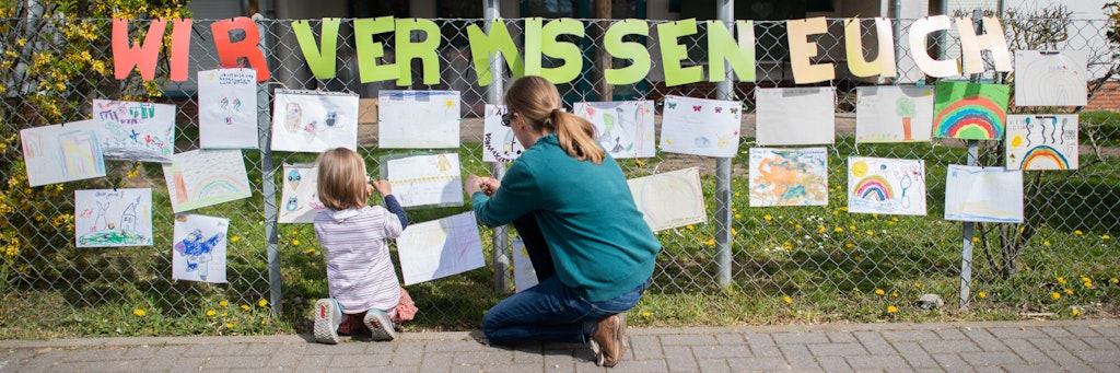 Eine Mutter befestigt mit ihrer Tochter ein selbstgemaltes Bild am Zaun eines geschlossenen Kindergartens. Bildfunk +++