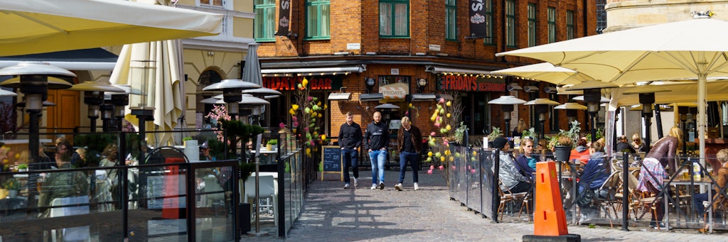 Schwedischer Sonderweg: Die Menschen sitzen in Restaurants und Cafés auf Lilla Torg Platz im schwedischen Malmö in der Sonne.
