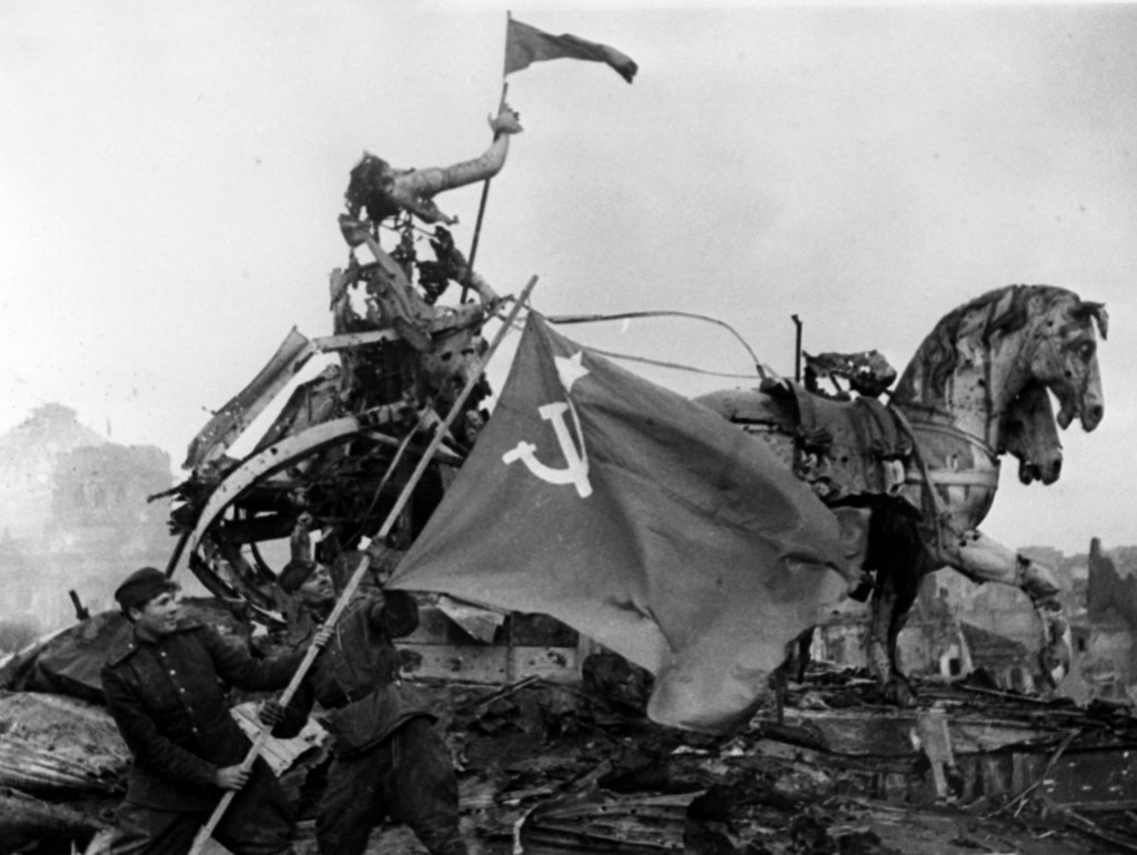 Auf dem Brandenburger Tor weht die Rote Fahne, links im Hintergrund steht die Ruine des Reichstags. Als der Kriegsberichterstatter Jewgenij Chaldej dieses Foto komponiert, wird um das Gebäude noch gekämpft.