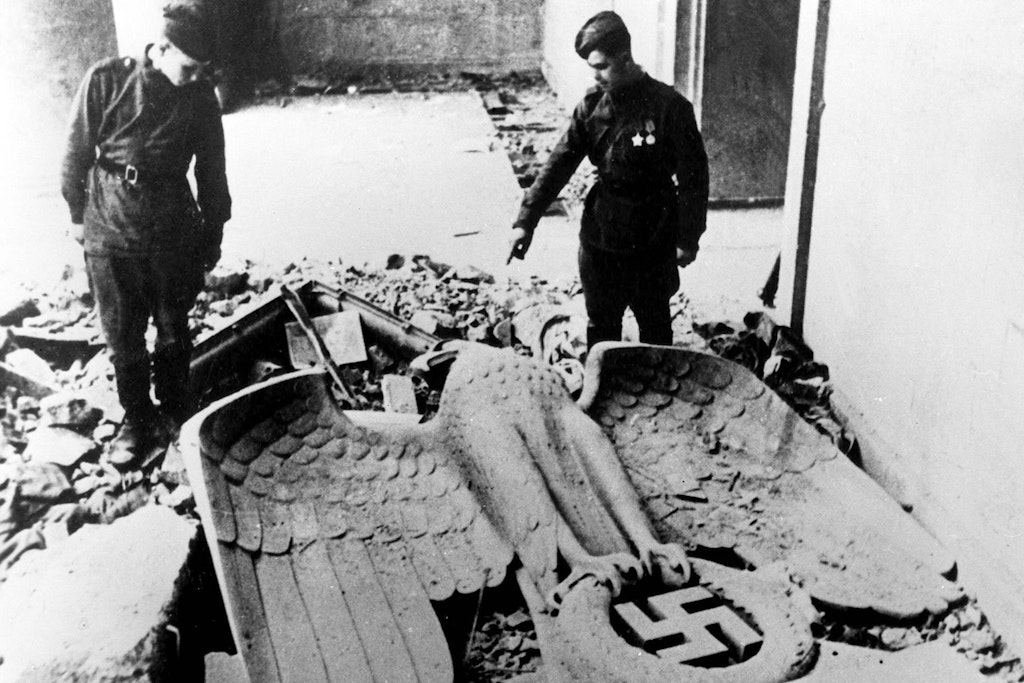 Zwei sowjetische Soldaten stehen an der Reichskanzlei vor einem am Boden liegenden steinernen Reichsadler.