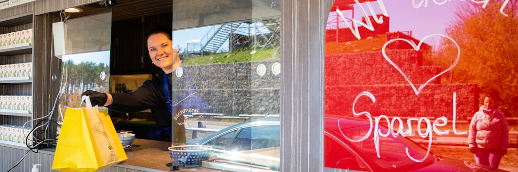 Restaurant-Mitarbeiterin Aline hält im Fenster des Drive-In-Schalters in Klaistow eine Papiertüte mit Schnitzel und Spargel.