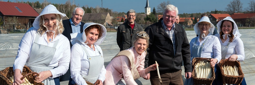 Beelitz: Spargelkönigin Gina-Luise Schrey (Mi.) sticht zum offiziellen Saisonstart auf dem Josef Jakobs Spargel Hof den ersten Beelitzer Spargel. Neben ihr stehen Landwirt Josef Jakobs und die Spargelfrauen. 
