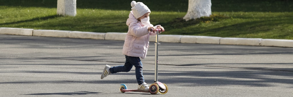 Ein Mädchen mit Mundschutz führt Roller.