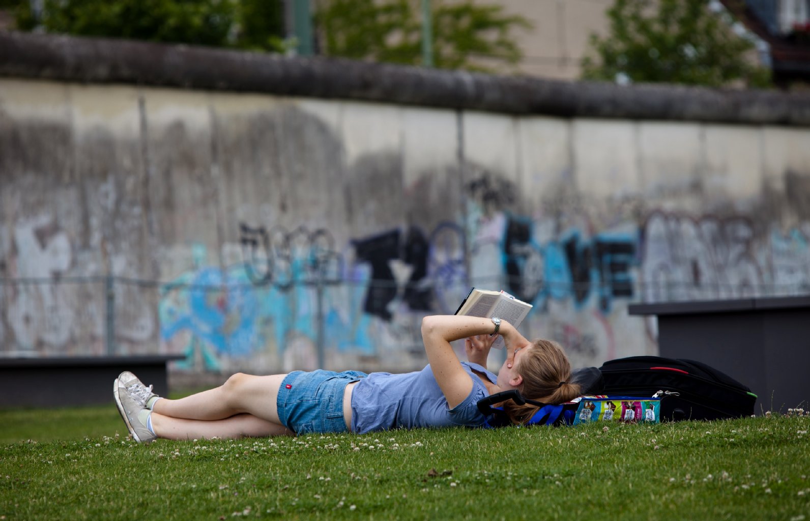 Eine Frau liest in Berlin vor der Mauer in der Bernauerstrasse ein Buch.