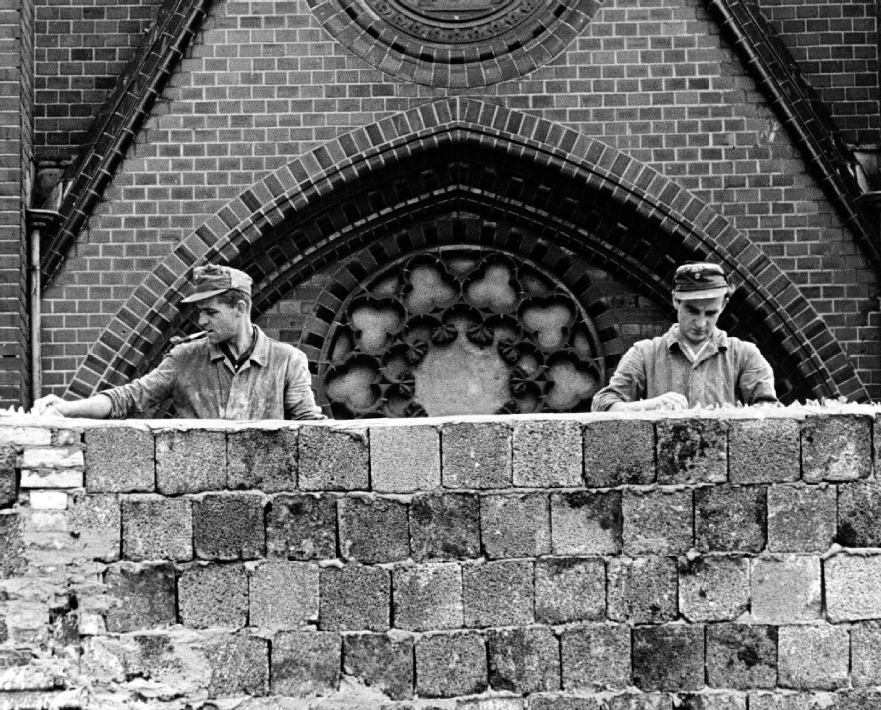 Ostberliner Arbeiter bewehren die Krone der Mauer in Berlin mit Glassplittern.