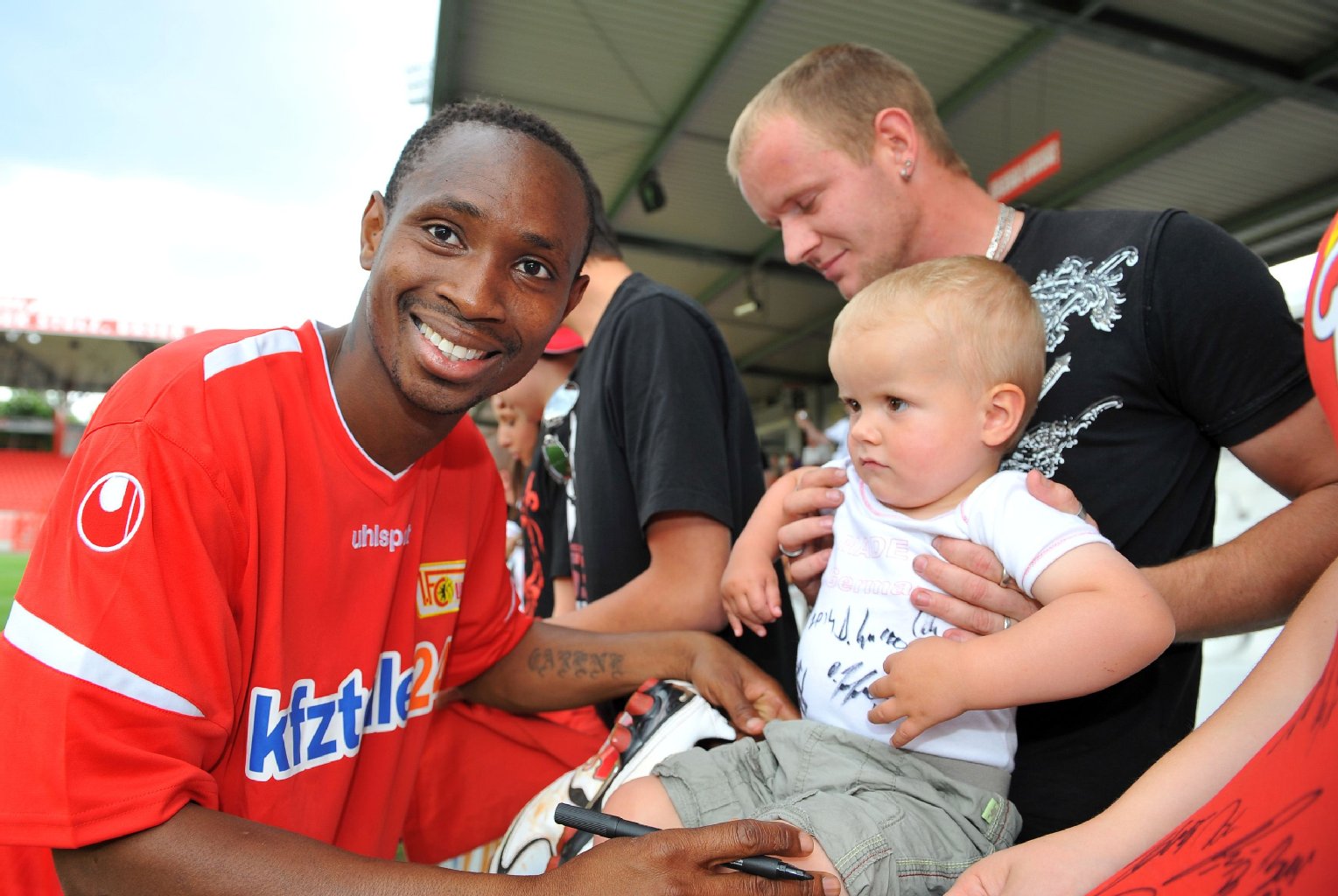 Patrick Zoundi lacht beim Autogrammeschreiben.