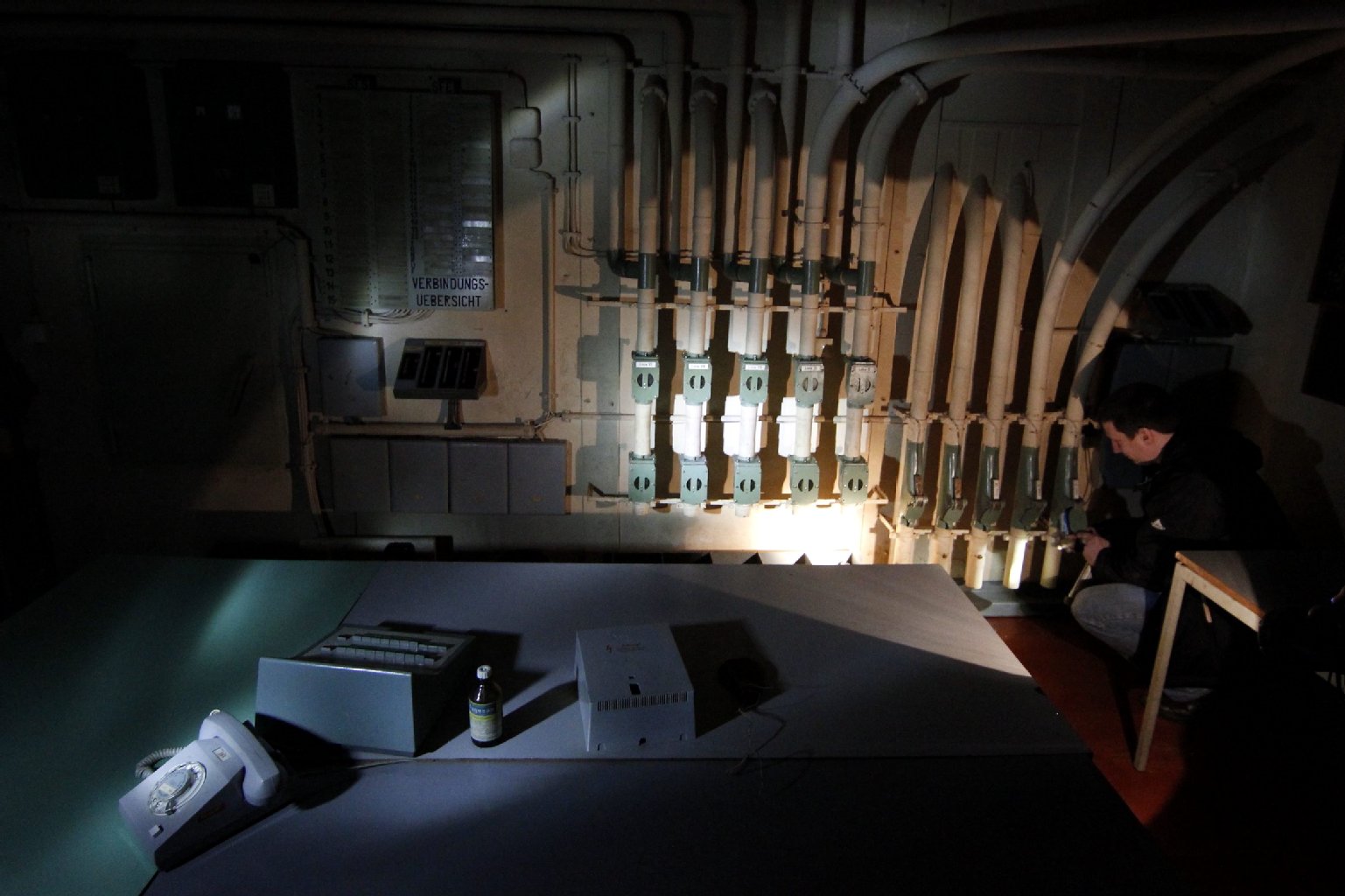 Bunkerforscher Hannes Hensel kniet im Licht einer Taschenlampe vor der Rohrpostanlage des Bunkers.