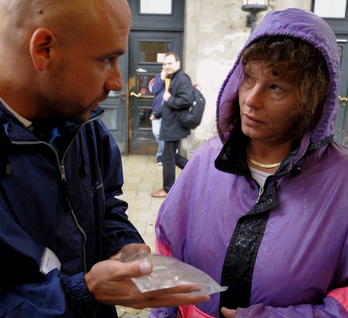 Ein Mitarbeiter der Berliner Wasserbetriebe unterhält sich vor dem Rathaus in Berlin-Spandau an einem Stand mit "Notfallbeutel" mit sauberem Trinkwasser mit einer Passantin.