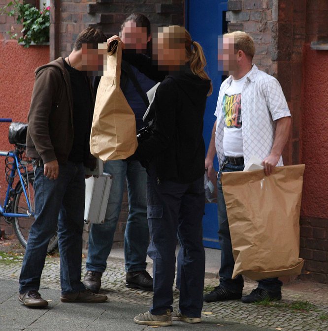 Ermittler der Berliner Polizei mit zwei braunen Papiertüten, in denen sie private Gegenstände der Verdächtigen gesichert haben.