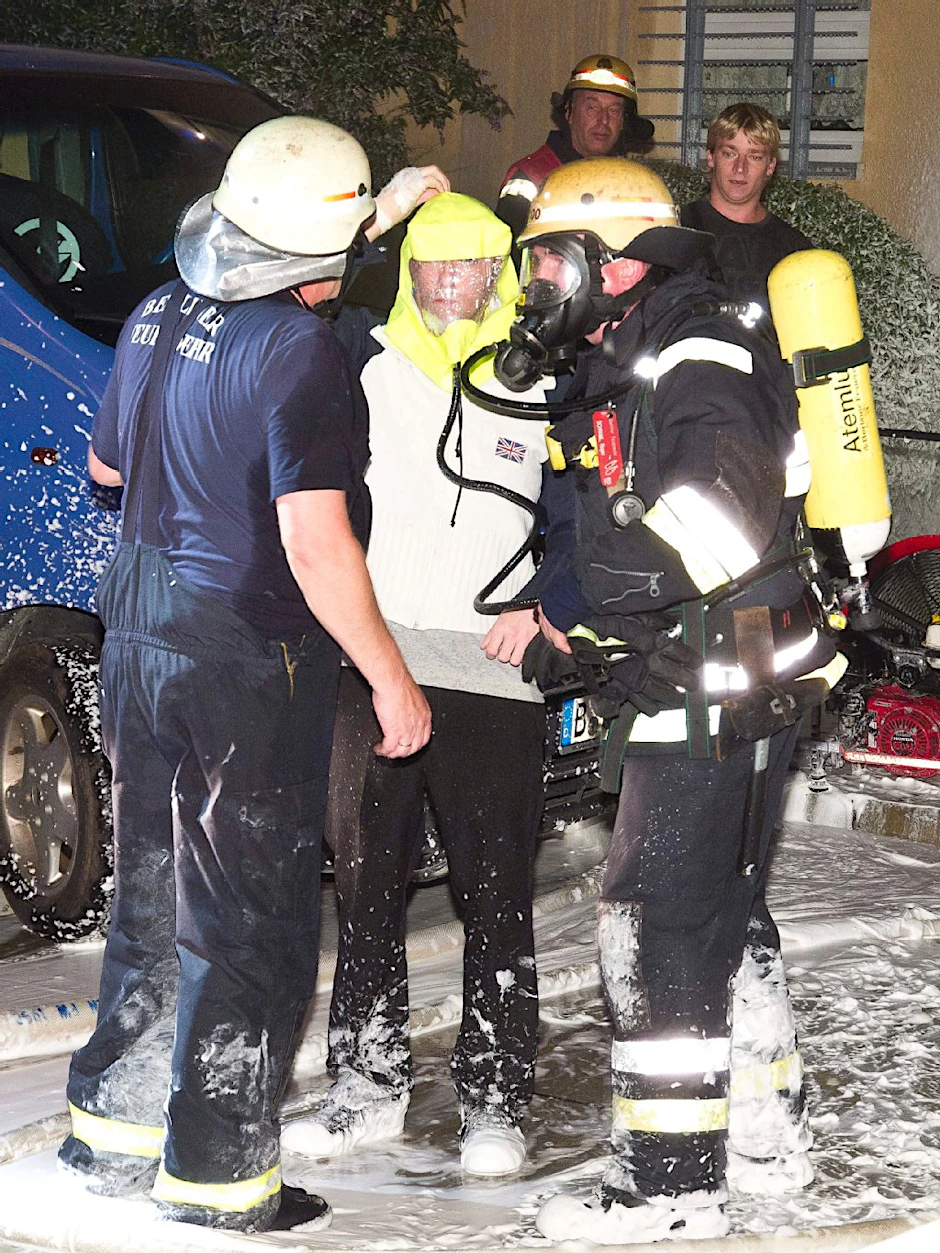 Zwei Feuerwehrler haben einem Hausbewohner eine Rettungshaube übergezogen, versorgen ihn so mit Sauerstoff.