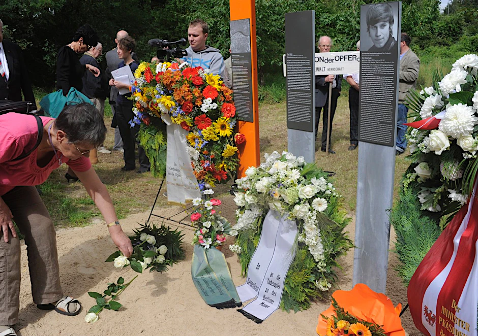 Eine Frau legt an der Stele in Teltow eine Rose für die beim Fluchtversuch erschossenen Peter Mädler und Karl-Heinz Kube nieder.