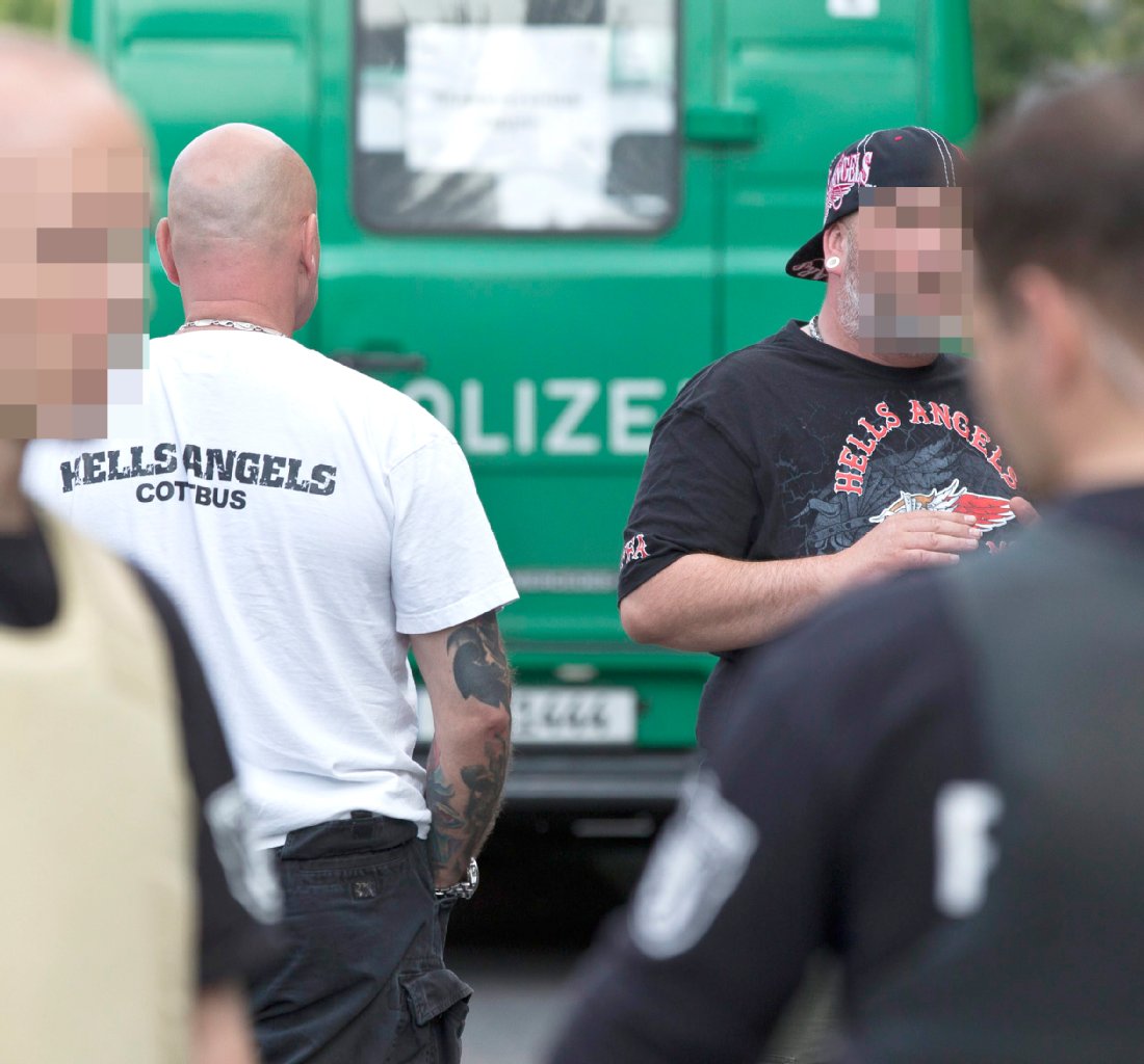 Zwei Mitglieder der Hells Angels, im Hintergrund ist ein Polizeiwagen zu sehen.