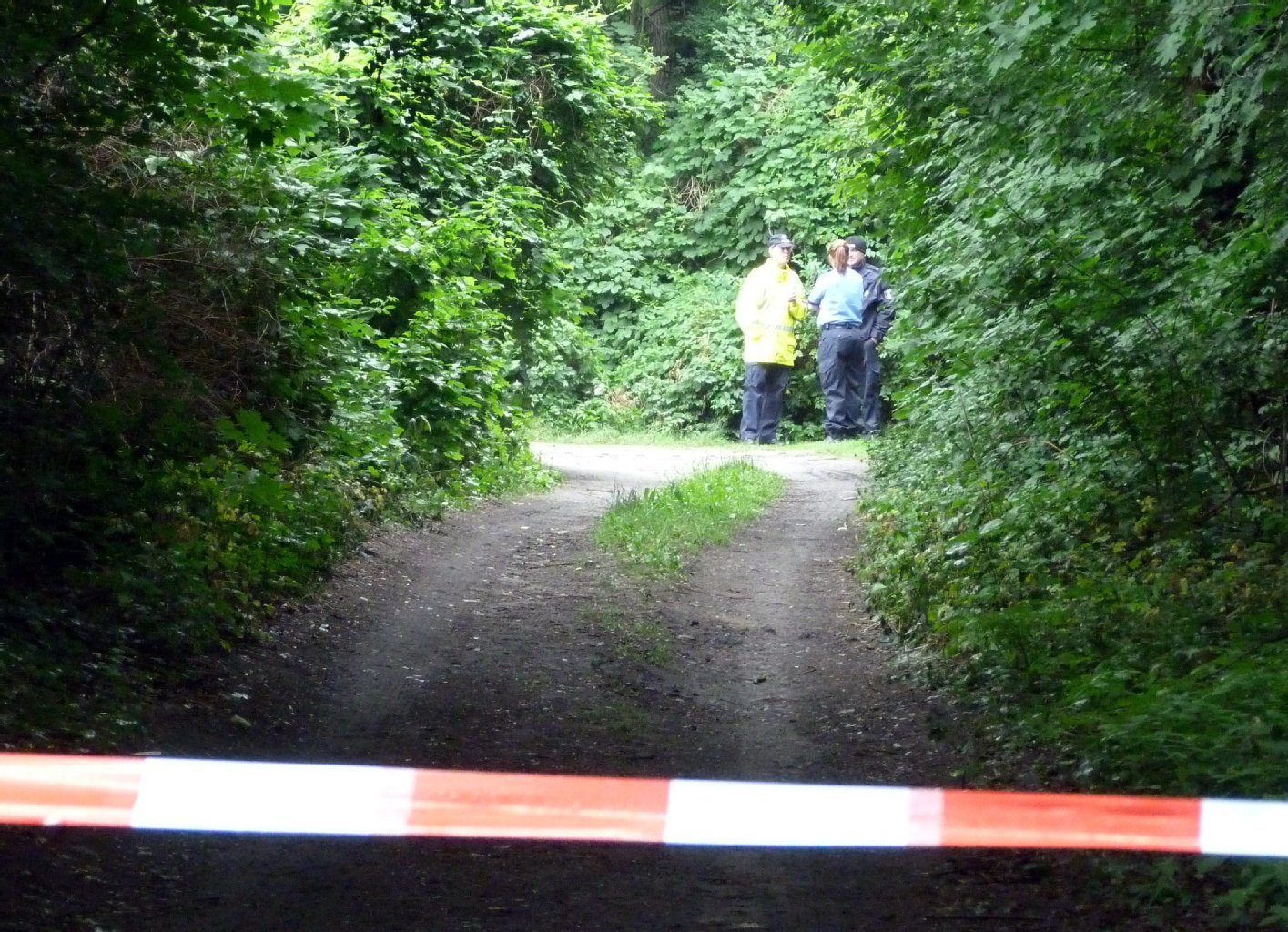 Ermittler der Polizei stehen an der Stelle, an der die Leiche der hübschen Blondine gefunden wurde.