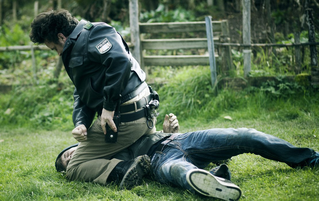 Einen nimmt er noch: Polizist Georg Zimmermann (Sascha Alexander Gersak) verteilt großzügig seine staatliche Fürsorge, während Ganove David Kleinert (Fabian Halbig) schon genussvoll die Augen geschlossen hat.