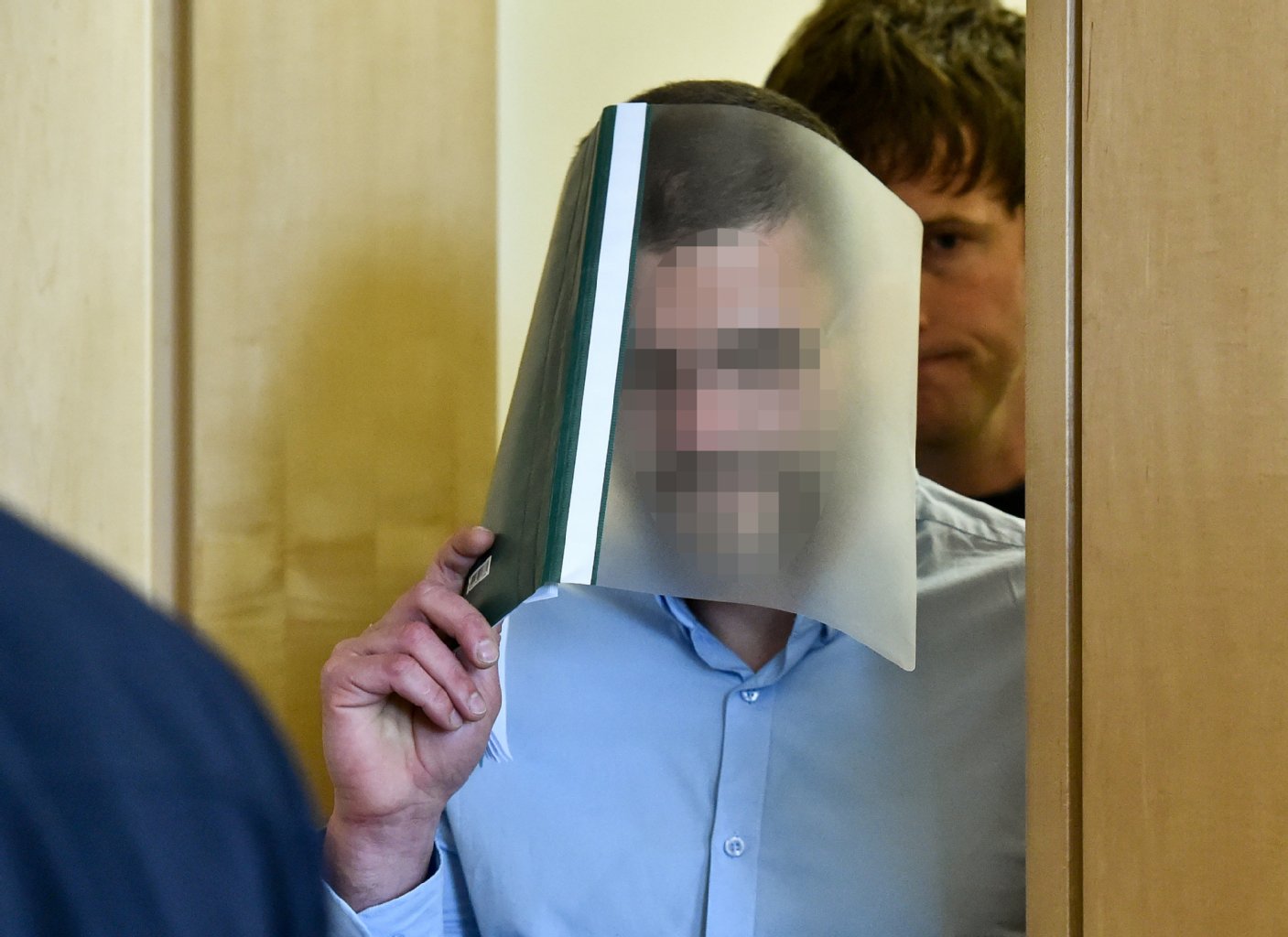 Erst Maske, jetzt Mappe: Mario K. (46) versteckt sein Gesicht zum Prozessauftakt. Er soll als „Maskenmann“ zweimal eine Millionärsfamilie überfallen und einen Investmentbanker entführt sowie erpresst haben.