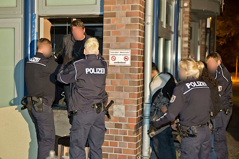 Polizisten bringen einen Einbrecher aus der Kneipe. Sein Komplize steht bereits draußen an der Wand.