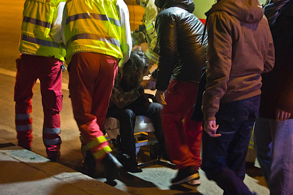 Zusammengesunken sitzt die Mutter der vermissten 21-Jährigen in einem Rollstuhl der Feuerwehr. Ein Bekannter hält tröstend ihre Hand.