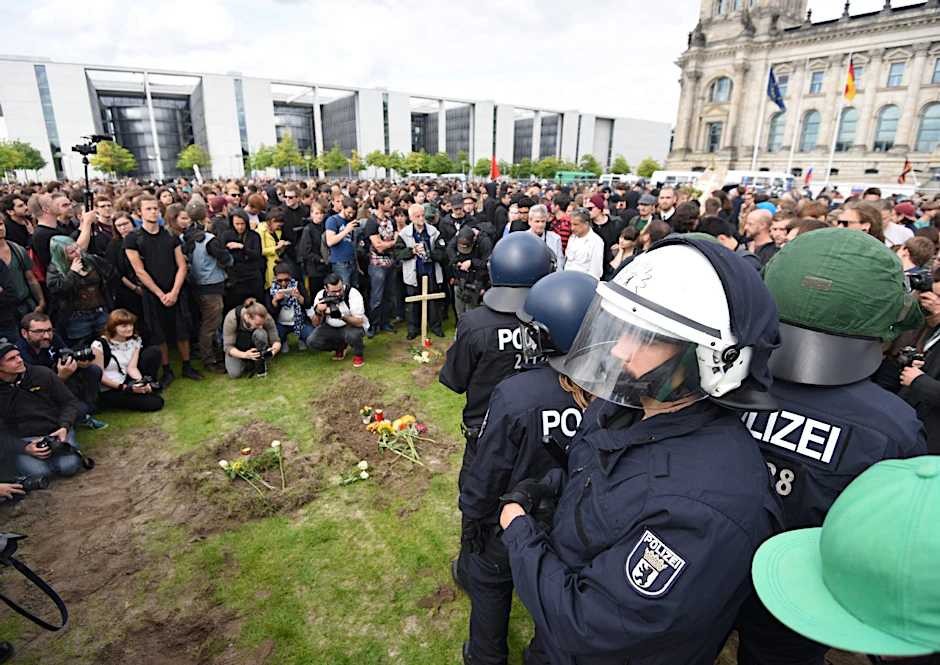 Demo-Teilnehmer auf der Grünanlage vor dem Reichstag. Polizisten schirmen das restliche Gelände ab.