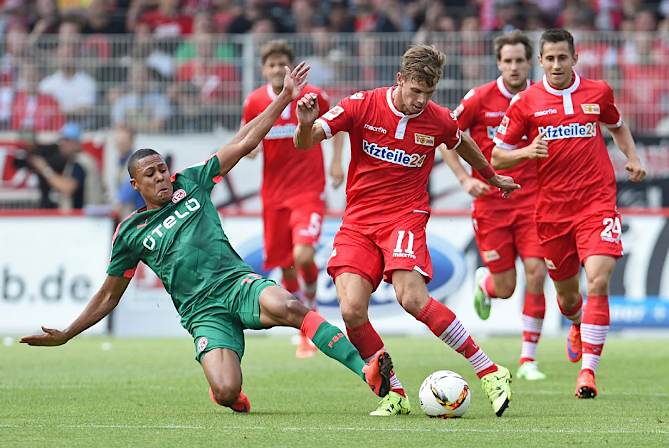 Mathis Bolly von Fortuna Düsseldorf grätscht Maximilian Thiel von Union Berlin.