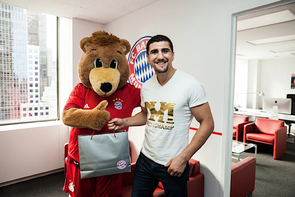 Marco Huck strahlt mit Bayern-Maskottchen Berni im New Yorker Fanshop um die Wette.
