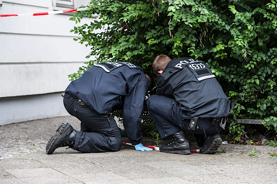 Polizisten suchen in einem Gebüsch am Olivaer Platz nach der Tat nach Spuren der Täter.