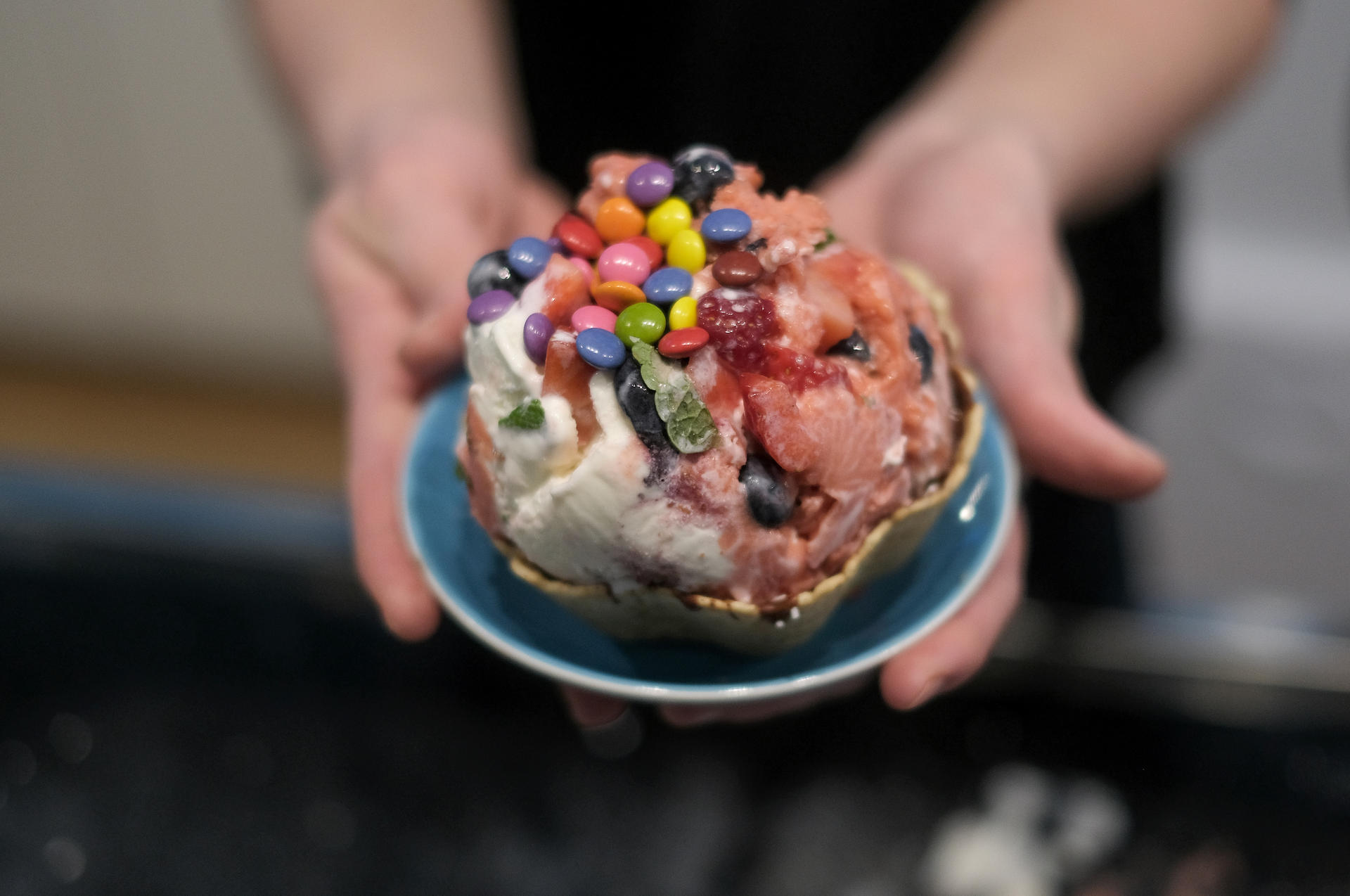 Minze, Erdbeeren und Blaubeeren sind mit einer Portion Erdbeer- und Joghurteis auf einem kalten Stein zu einer Eiskugel geformt und mit Schokolinsen garniert worden.  