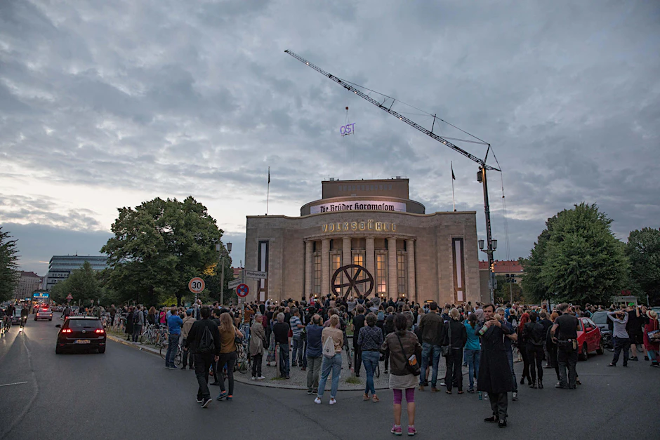 Vor der Volksbühne hat sich eine Menschenmenge versammelt, sieht dem Abbau des Schriftzugs zu.