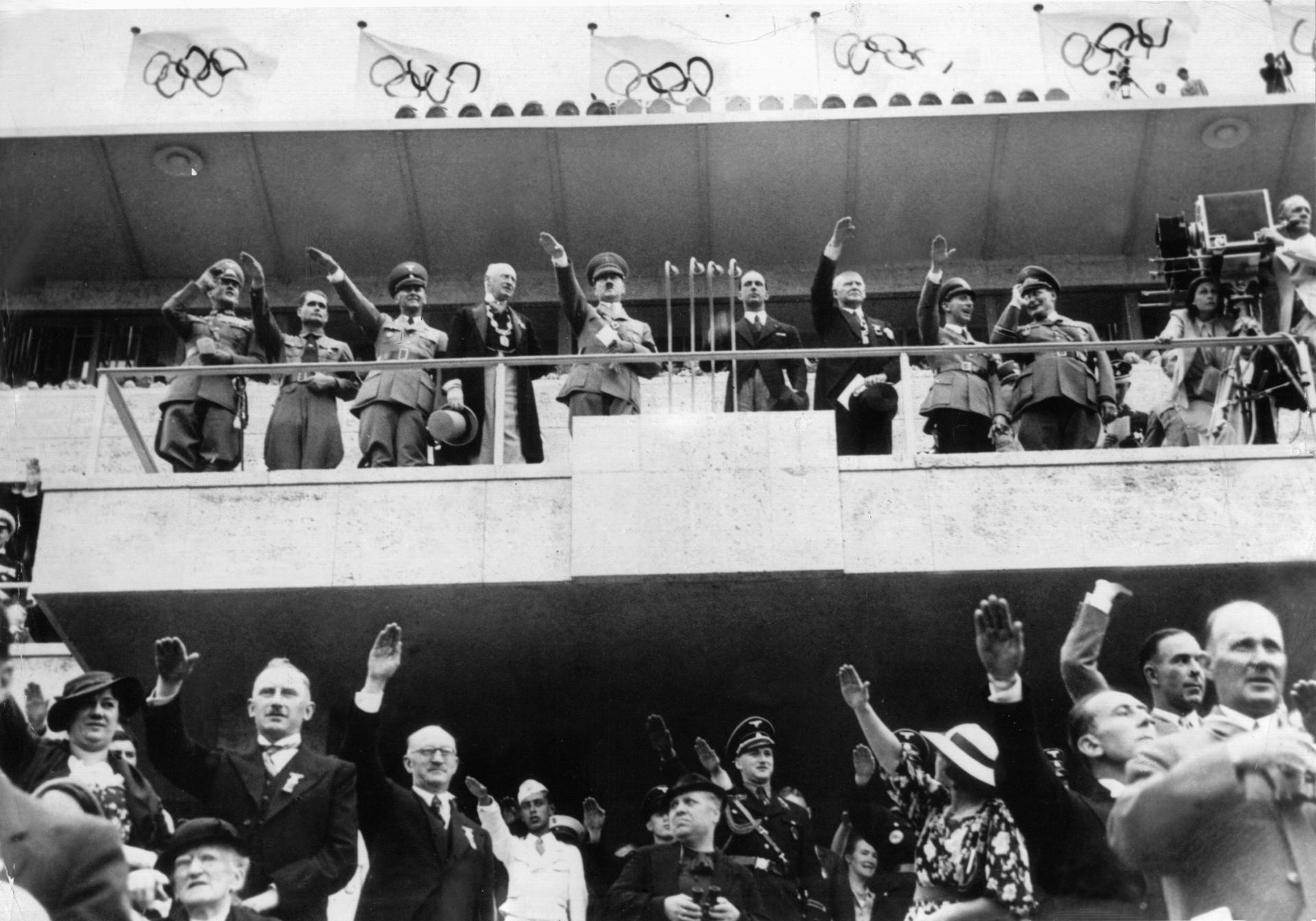 Adolf Hitler (M) bei der Eröffnung der XI. Olympischen Spiele mit Rudolf Heß (2.v.l.), Joseph Goebbels (8.v.l.), Hermann Göring (9.v.l.) und Leni Riefenstahl (r) an der Kamera.