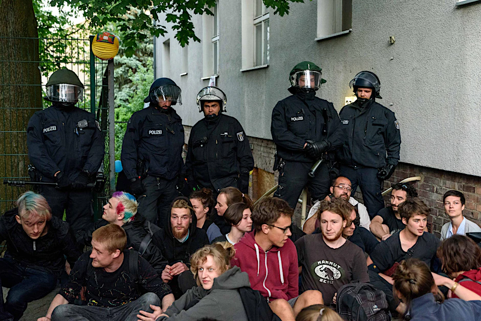 Polizisten sichern das besetzte Haus. Davor sitzen Protestierende, die die Hausbesetzer unterstützt haben. 