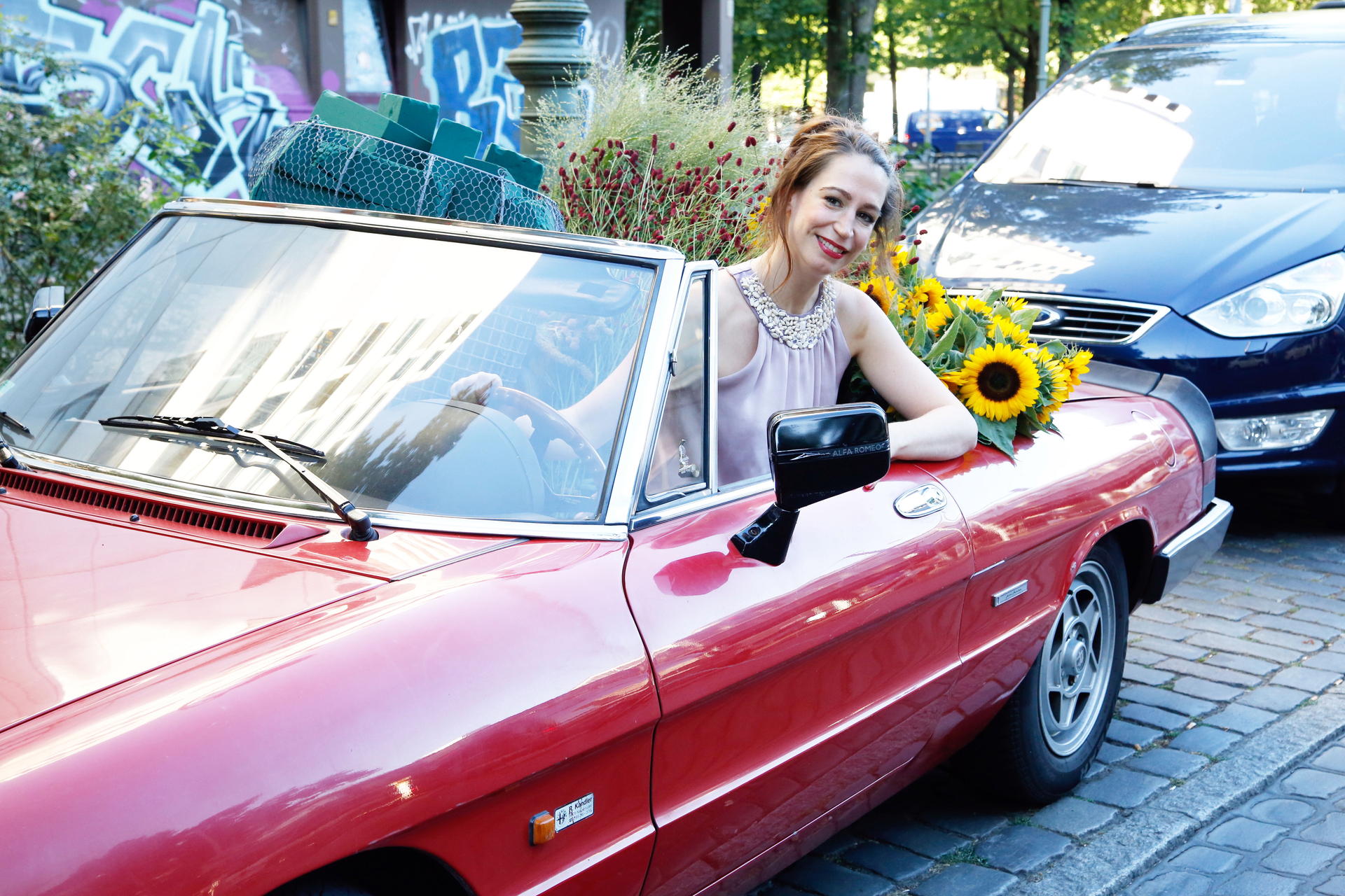 In ihrem roten Cabrio kommt Mona zum Kotti, auf dem Rücksitz stapeln sich Blumen.