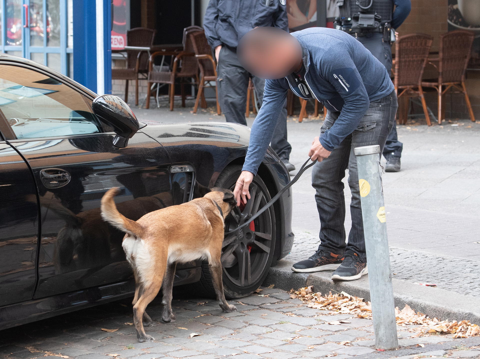 Ein Polizist untersucht mit einem Spürhund ein verdächtiges Fahrzeug. 