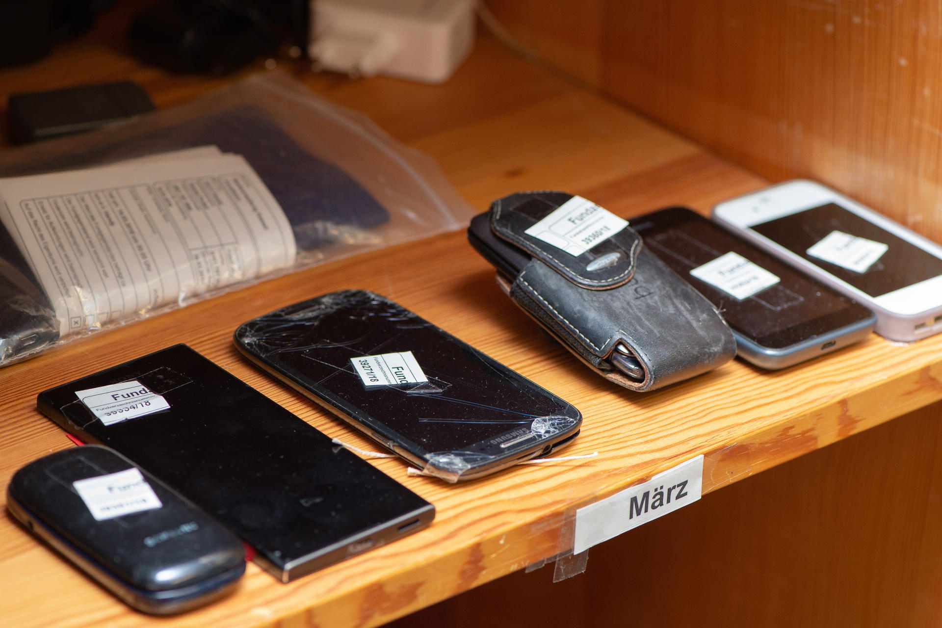 Mobiltelefone und Smartphones liegen in einer Vitrine. 