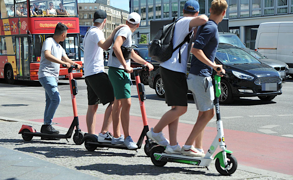 Fünf junge Männer teilen sich in Mitte drei E-Scooter. Das Fahren zu zweit ist verboten.