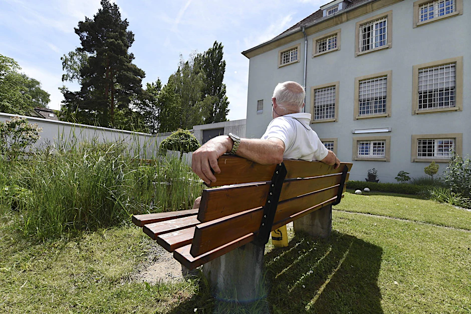 Sieht aus wie in einem Park, ist aber der Gefängnishof der JVA Singen. Ein verurteilter Senior genießt auf einer Bank die Sonnenstrahlen.