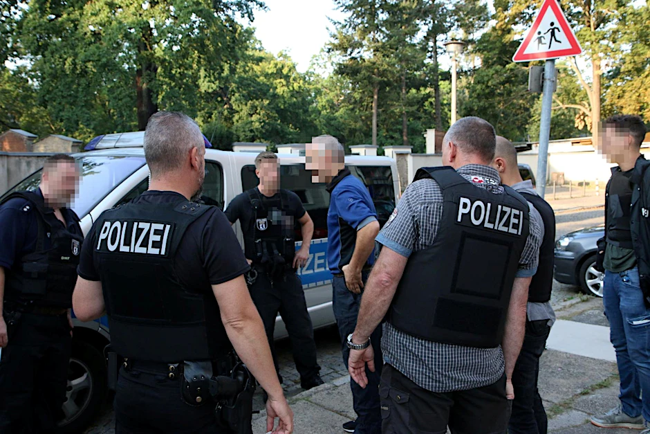 Razzia wegen möglicher Brandstiftung im Waldgebiet: Umringt von Polizisten steht der 43-Jährige vor seiner Wohnung.  