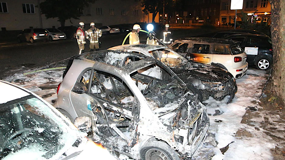 Einsatzkräfte der Feuerwehr an den ausgebrannten Autowracks in Lichtenberg. 