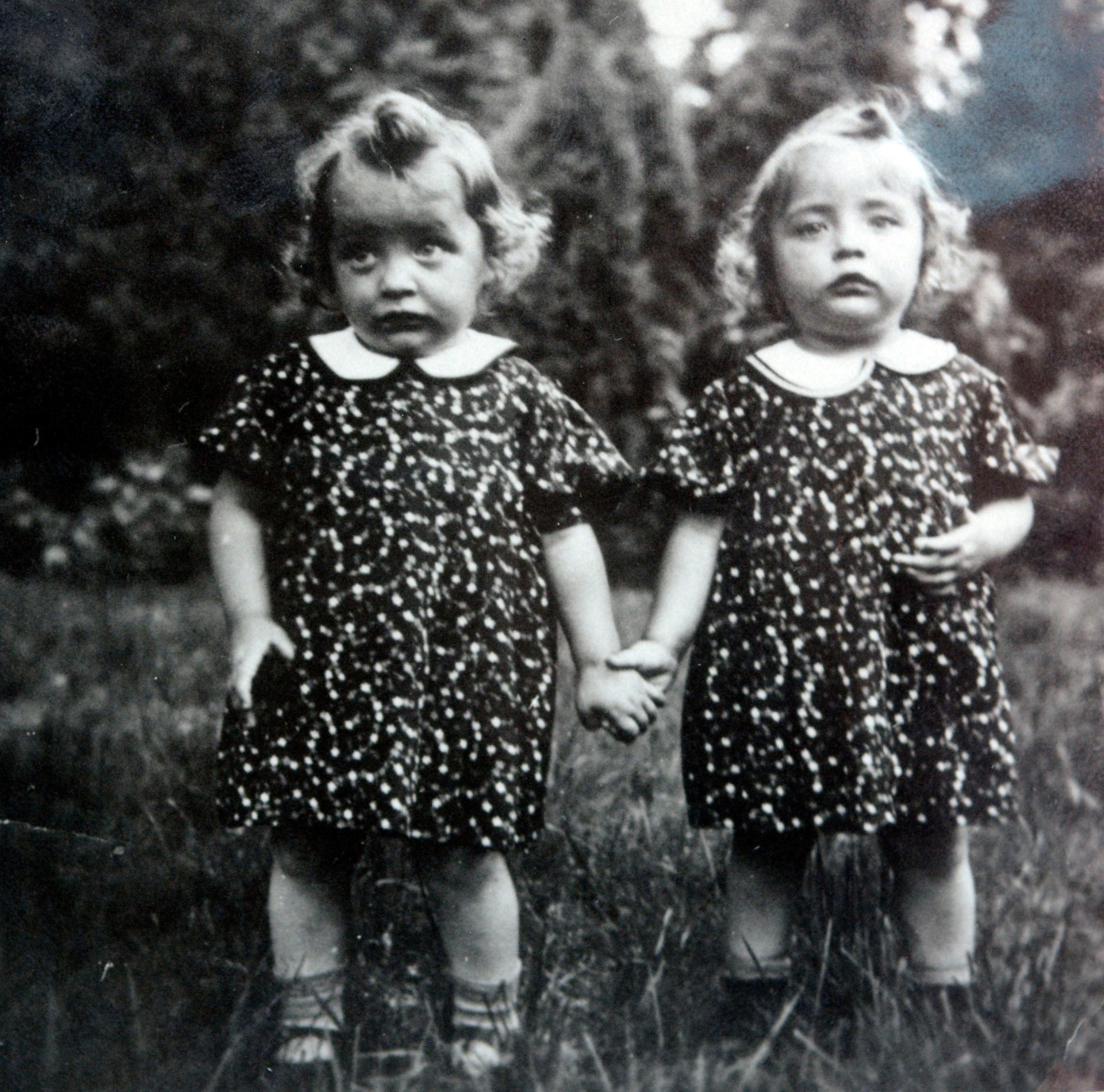 Vor 80 Jahren: Brigitte (li.) und Ingrid spazieren als Kleinkinder Hand in Hand über eine Blumenwiese.