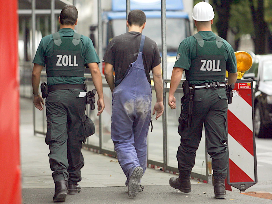 Zollbeamte haben auf einer Baustelle im Berliner Stadtteil Mitte einen dort tätigen Mann in die Mitte genommen und geleiten ihn zur Befragung.