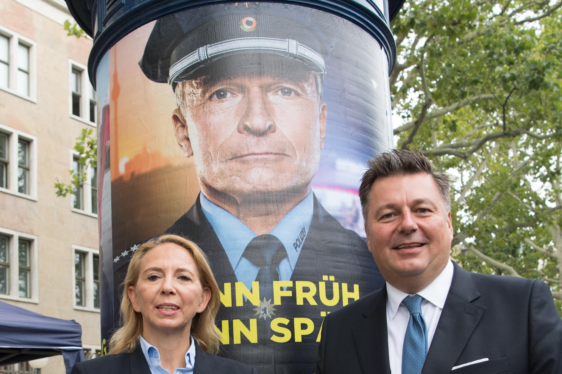Barbara Slowik, Polizeipräsidentin von Berlin, und Andreas Geisel (SPD), Innensenator von Berlin, stehen bei der Vorstellung der neuen Imagekampagne der Berliner Polizei vor einer Litfaßsäule mit einem der zugehörigen Plakate.