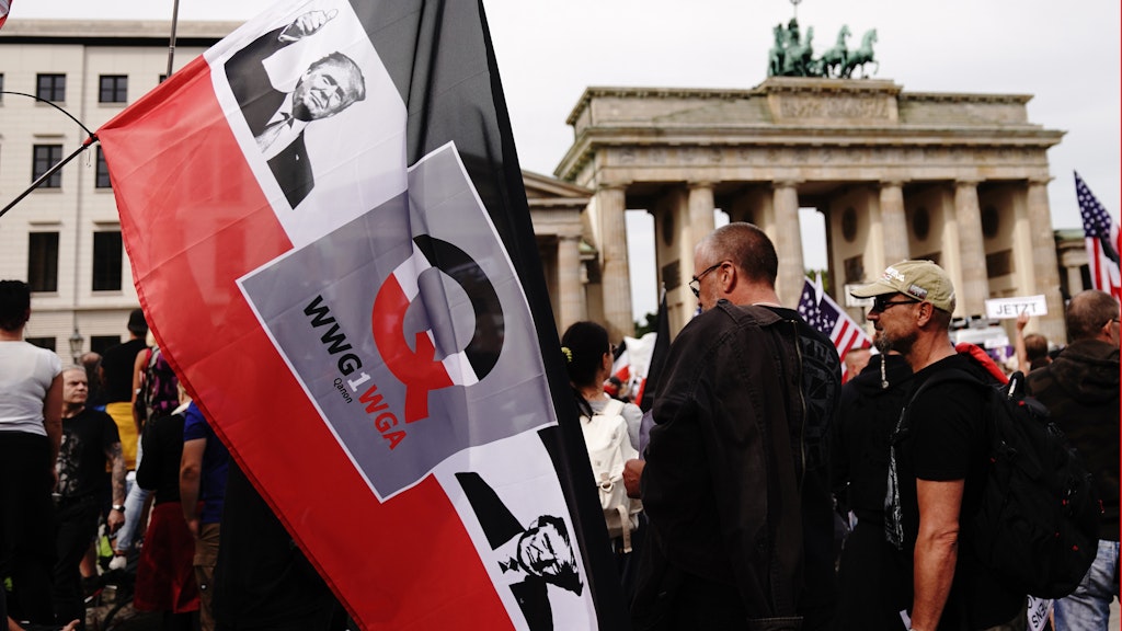 Demoteilnehmer in Berlin mit einer schwarz-weiß-roten Fahne, die ein Q trägt, das geheimnisvoll wirkende Kürzel WWG1WGA - und zwei Porträts von Donald Trump.