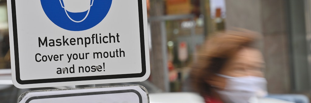 Ein Schild mit der Aufschrift „Maskenpflicht - Cover your mouth and nose!“ steht in einer Fußgängerzone in München.