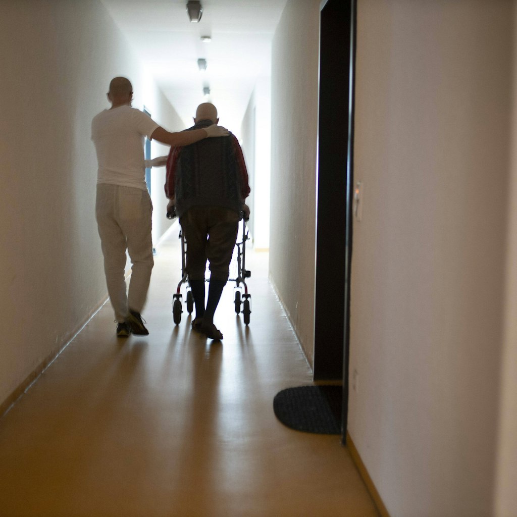 Ein Altenpfleger und Mann mit Rollator im Hausflur. Wie gehen die Heime in den Winter mit Corona?