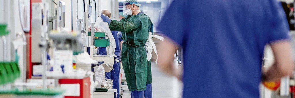 Krankenpfleger bekleiden sich mit Schutzkleidung vor einem Krankenzimmer auf einer Intensivstation. Noch sind viele für Covid-19-Patienten reservierte Betten in Berliner Krankenhäusern nicht belegt, doch die Lage verschärft sich Tag für Tag.