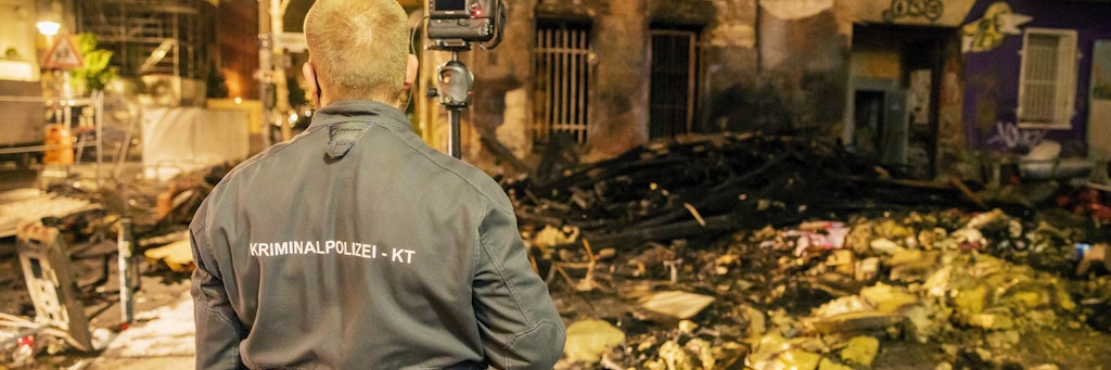 Nach einem Brand vor dem Haus Liebig34 fotografiert ein Polizist die Überreste.